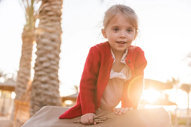 kleines Mädchen, das bei Sonnenuntergang am Strand spielt