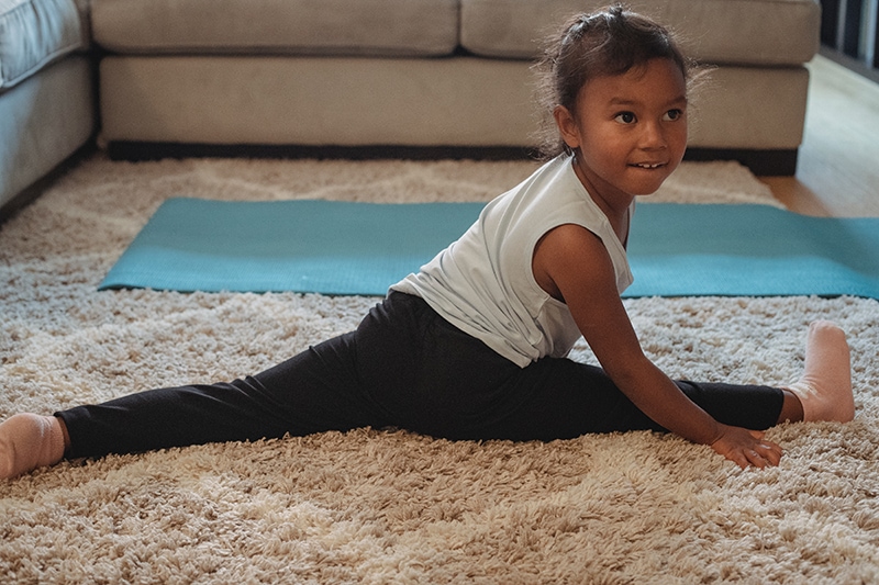 konzentriertes kleines Mädchen, das zu Hause auf dem Teppich spaltet