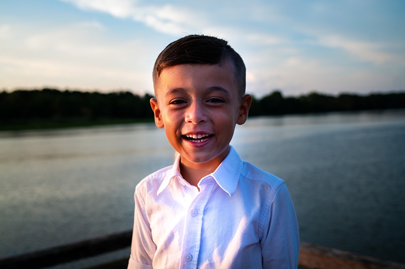 lächelnder Junge im weißen Hemd, der in der Nähe des Sees steht