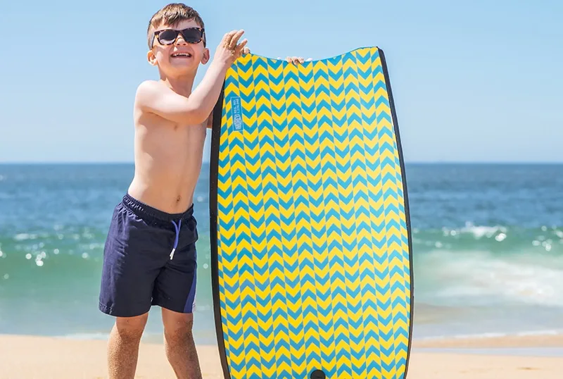 lächelnder Junge mit Surfbrett am Strand stehend