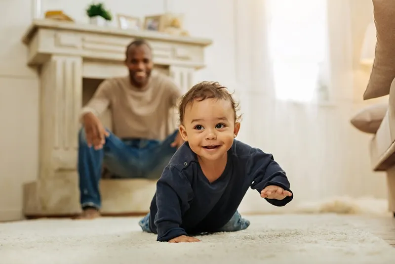 lächelndes Baby, das auf dem Boden krabbelt, während ihr Vater sie beobachtet