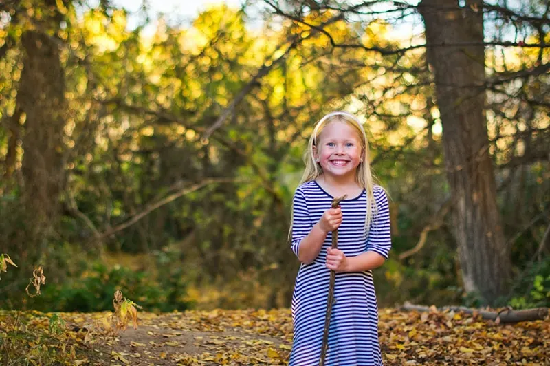 lächelndes kleines Mädchen, das im Wald steht und einen Stock hält