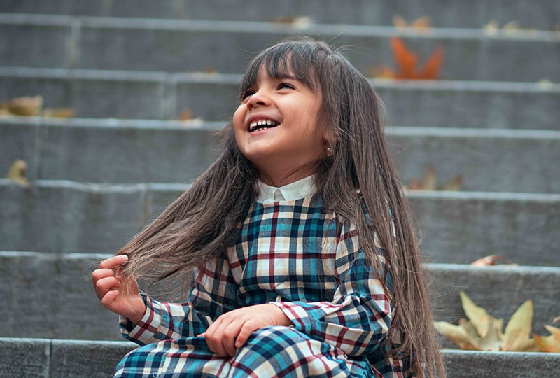lächelndes kleines Mädchen mit langen Haaren, das auf der Treppe sitzt