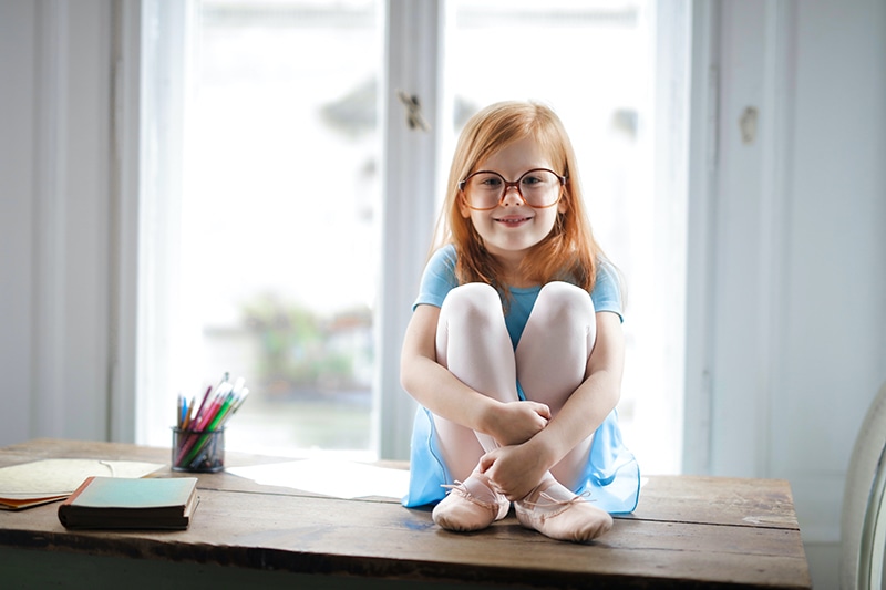 süßes kleines Mädchen mit Brille sitzt auf dem Tisch