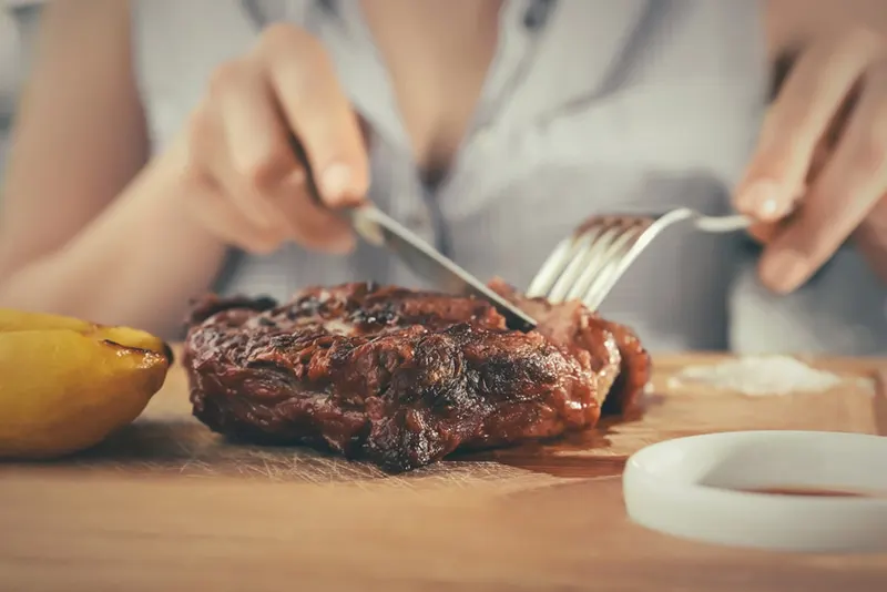Frau isst gegrilltes Steak auf Holzbrett im Restaurant