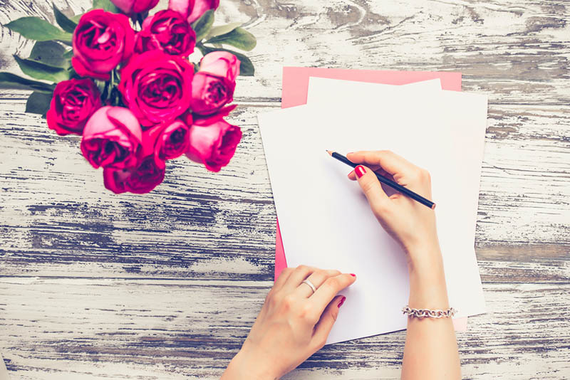 Frau schreibt auf einem weißen Papier mit Blumen auf dem Schreibtisch