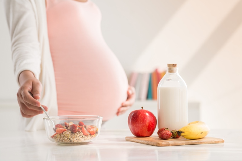 Schwangere Frau, die Mahlzeit mit Milch und Früchten zubereitet