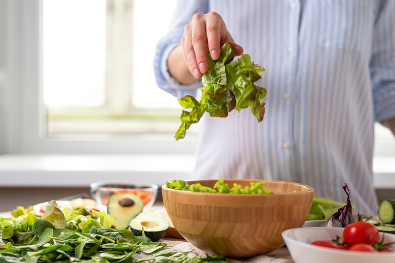 Schwangere Frau im blauen Hemd bereitet Salat aus dunkelgrünem Gemüse zu