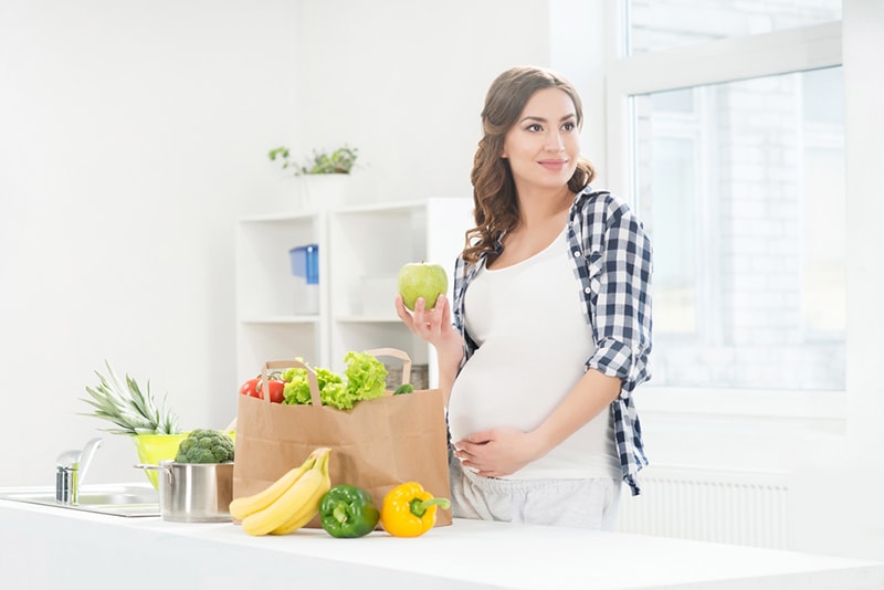 Schwangere Frau in der Küche, die Obst und Gemüse aus der Einkaufstasche auspackt