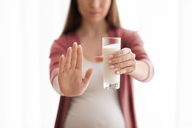 Schwangere Frau hält Glas Milch und zeigt Stoppgeste mit offener Handfläche