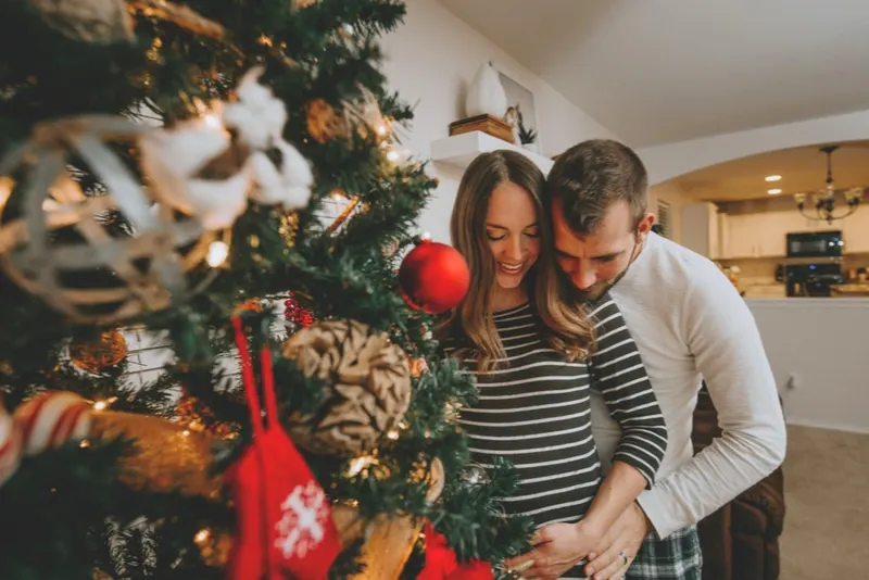 Schwangeres Paar steht vor Weihnachtsbaum