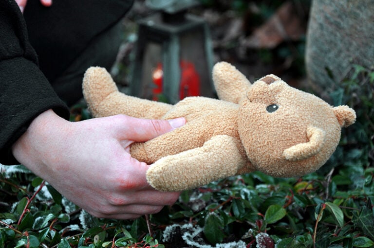 Person legt Teddybären auf Kindergrab