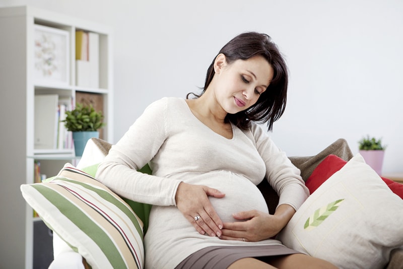 schwangere frau, die ihren bauch berührt, während sie zu hause sitzt