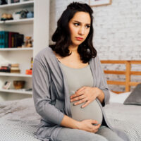 Übelkeit schwangere Frau sitzt auf dem Bett und hält sich den Bauch