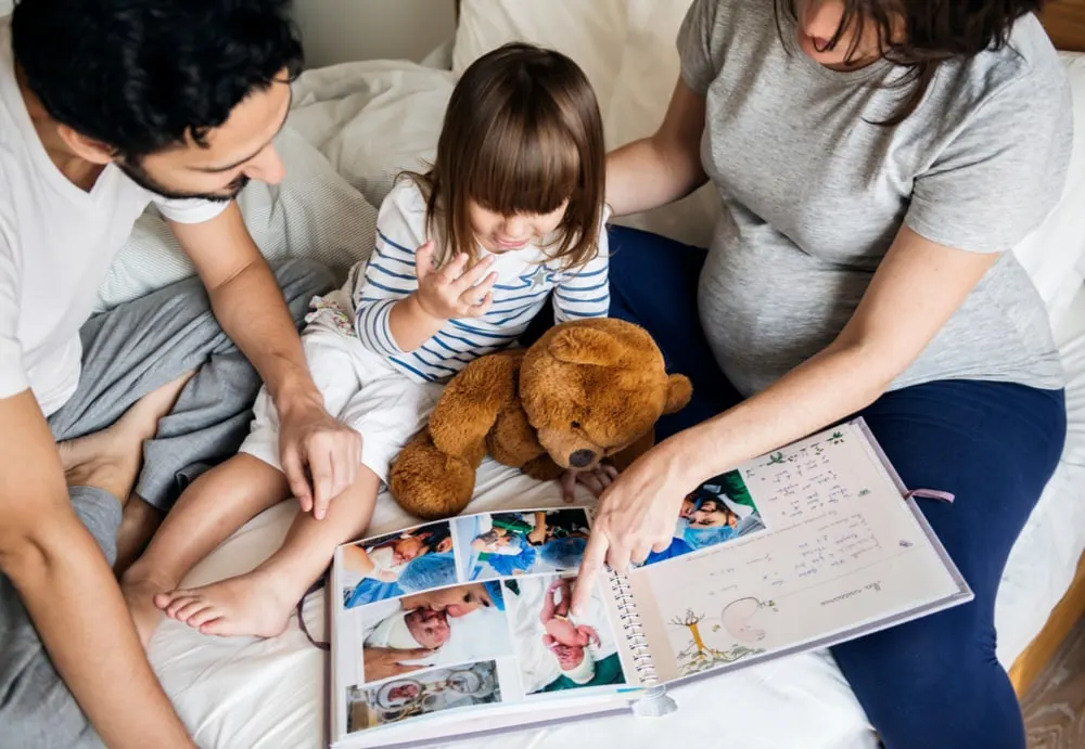 Eltern und Kind schauen sich ein Fotoalbum auf dem Bett an