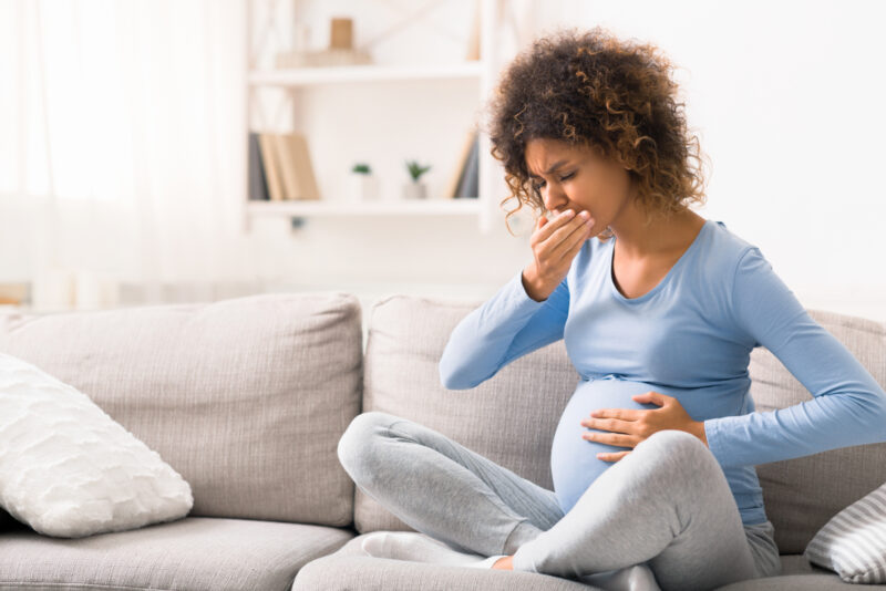 Kranke schwangere Frau sitzt auf dem Sofa