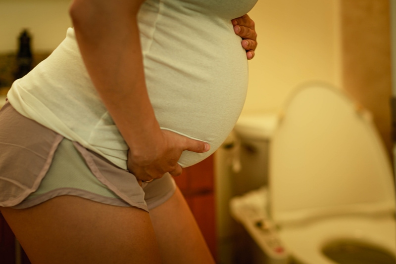 Schwangere Frau mit Blasenschwäche in der Toilette