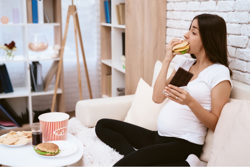 schwangere Frau sitzt und isst Hamburger mit Schokolade