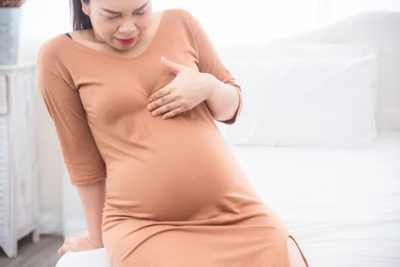 schwangere frau, die ihre brust vor schmerzen hält