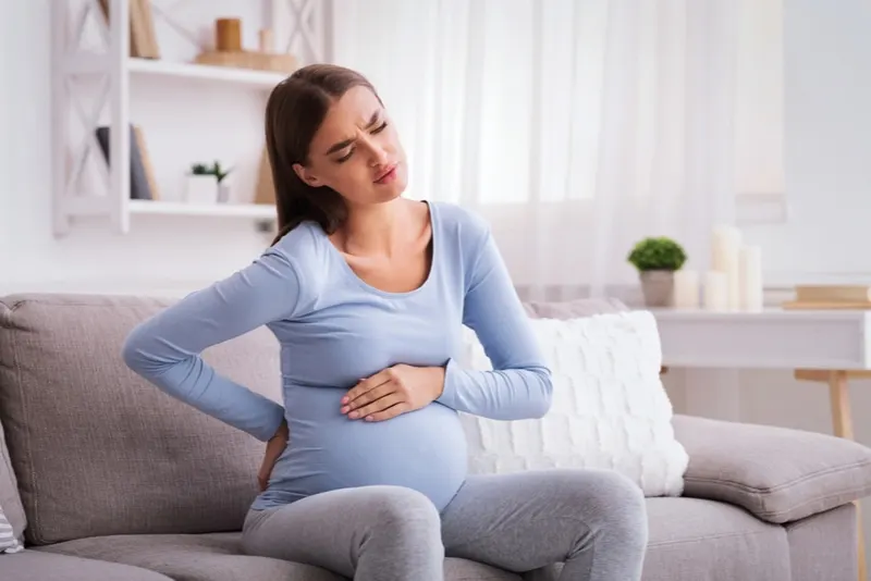 schwangere frau mit schmerzen, die auf der couch sitzt