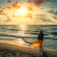 Frau geht bei Sonnenuntergang am Strand spazieren