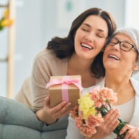 Tochter umarmt Mutter mit Geschenk und Blumen