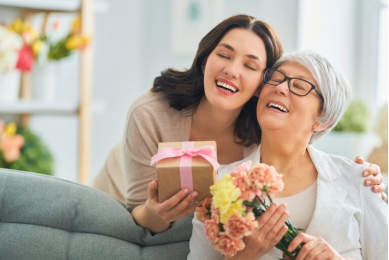 Tochter umarmt Mutter mit Geschenk und Blumen