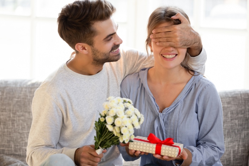 Mann überrascht seine Frau zum Geburtstag mit Blumen und Geschenk
