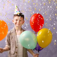 Kleiner Junge, der zu seinem Geburtstag mit Luftballons posiert