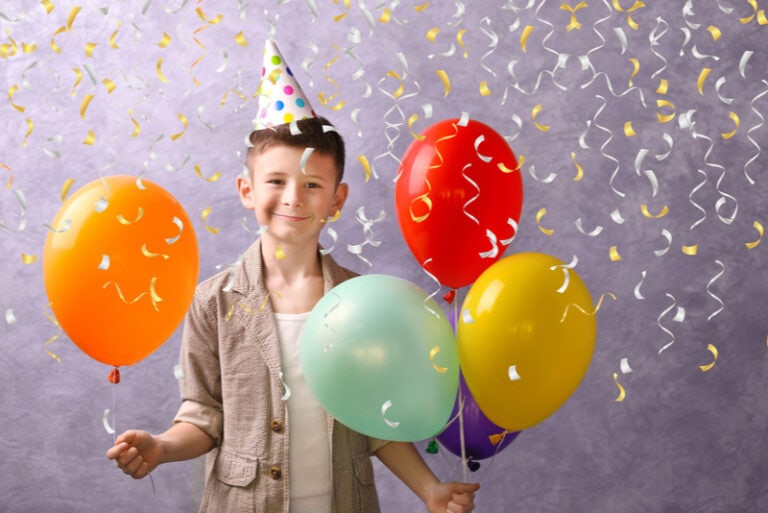 Kleiner Junge, der zu seinem Geburtstag mit Luftballons posiert