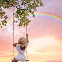 Frau schaukelt auf dem Schaukelstuhl und betrachtet den Regenbogen