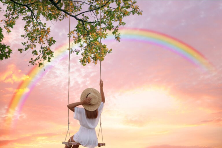 Frau schaukelt auf dem Schaukelstuhl und betrachtet den Regenbogen