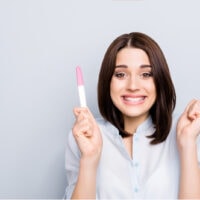glückliche, begeisterte Frau, die einen Schwangerschaftstest in der Hand hält