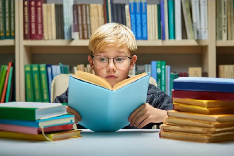 süßer kleiner Junge liest ein Buch in der Bibliothek