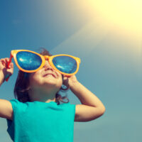 Glückliches kleines Mädchen mit großer Sonnenbrille, die die Sonne betrachtet