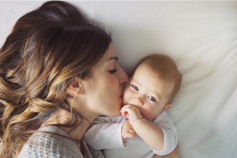Junge Mutter küsst ihr Baby im Bett