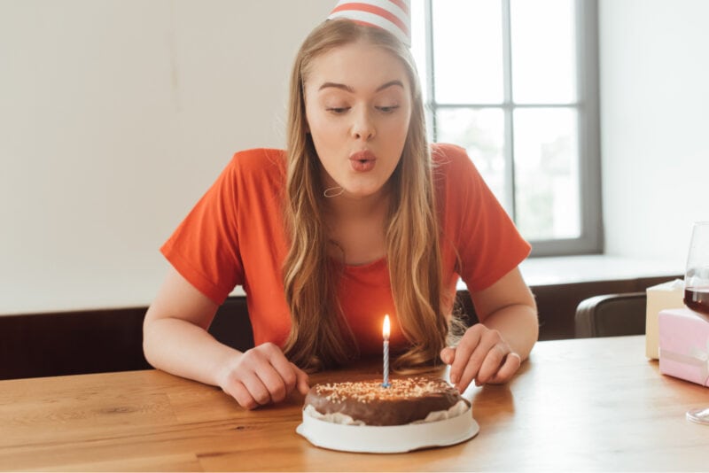 Blondes Mädchen bläst Kerze auf Kuchen aus