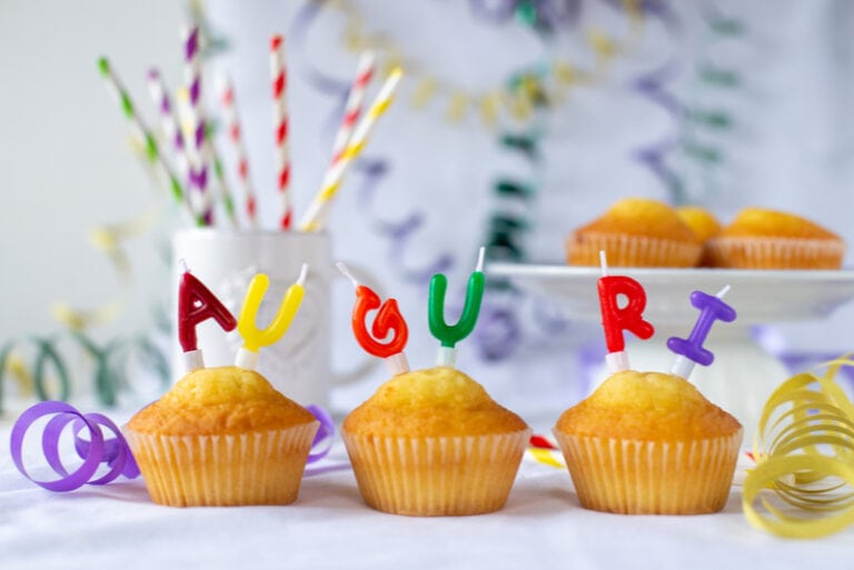Drei Muffins mit Kerzen und der Aufschrift AUGURI
