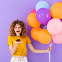 junge frau, die geburtstag mit bunten luftballons und stück kuchen feiert