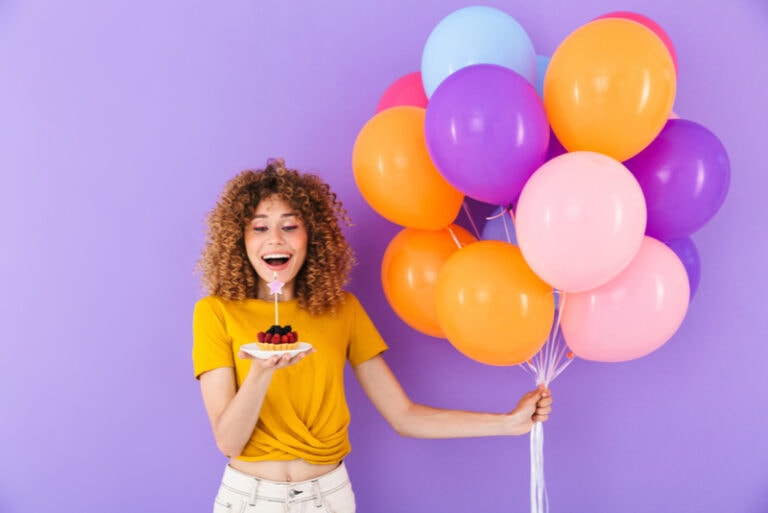junge frau, die geburtstag mit bunten luftballons und stück kuchen feiert