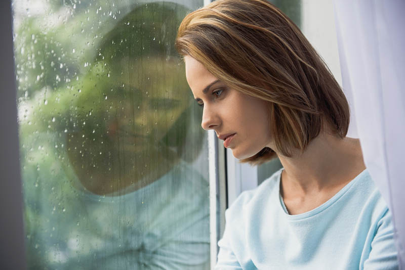 traurige Frau steht neben dem regnerischen Fenster