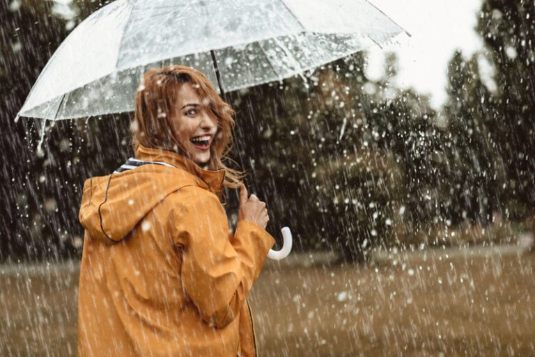 junge frau, die auf dem regen mit regenschirm lächelt