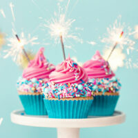 Drei Geburtstags-Cupcakes mit rosa Zuckerguss und Party-Wunderkerzen