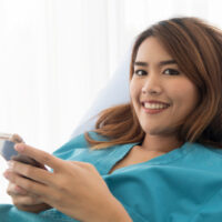 Glückliche junge Patientin, die Smartphone lächelt und hält