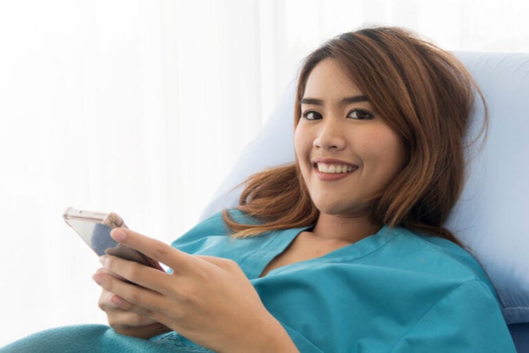 Glückliche junge Patientin, die Smartphone lächelt und hält