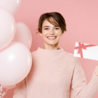 Frau lächelt und hält Geburtstagskarte und Luftballons