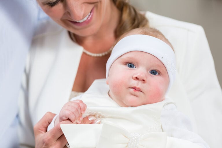 Patin hält Baby, das ein weißes Taufkleid trägt