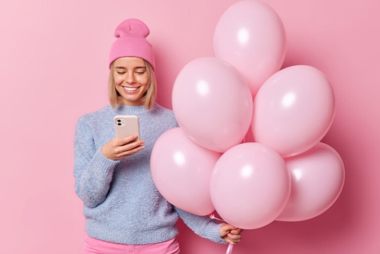 Frau nutzt Handy zum Online-Chat und hält einen Haufen aufgeblasener Luftballons