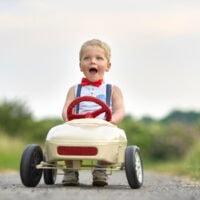 Aktiver kleiner Junge, der Tretauto im Sommergarten fährt