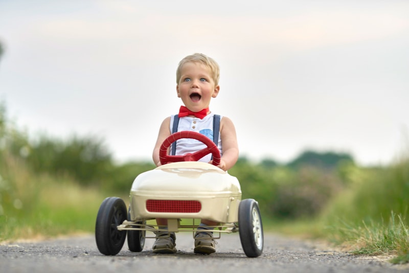 Aktiver kleiner Junge, der Tretauto im Sommergarten fährt